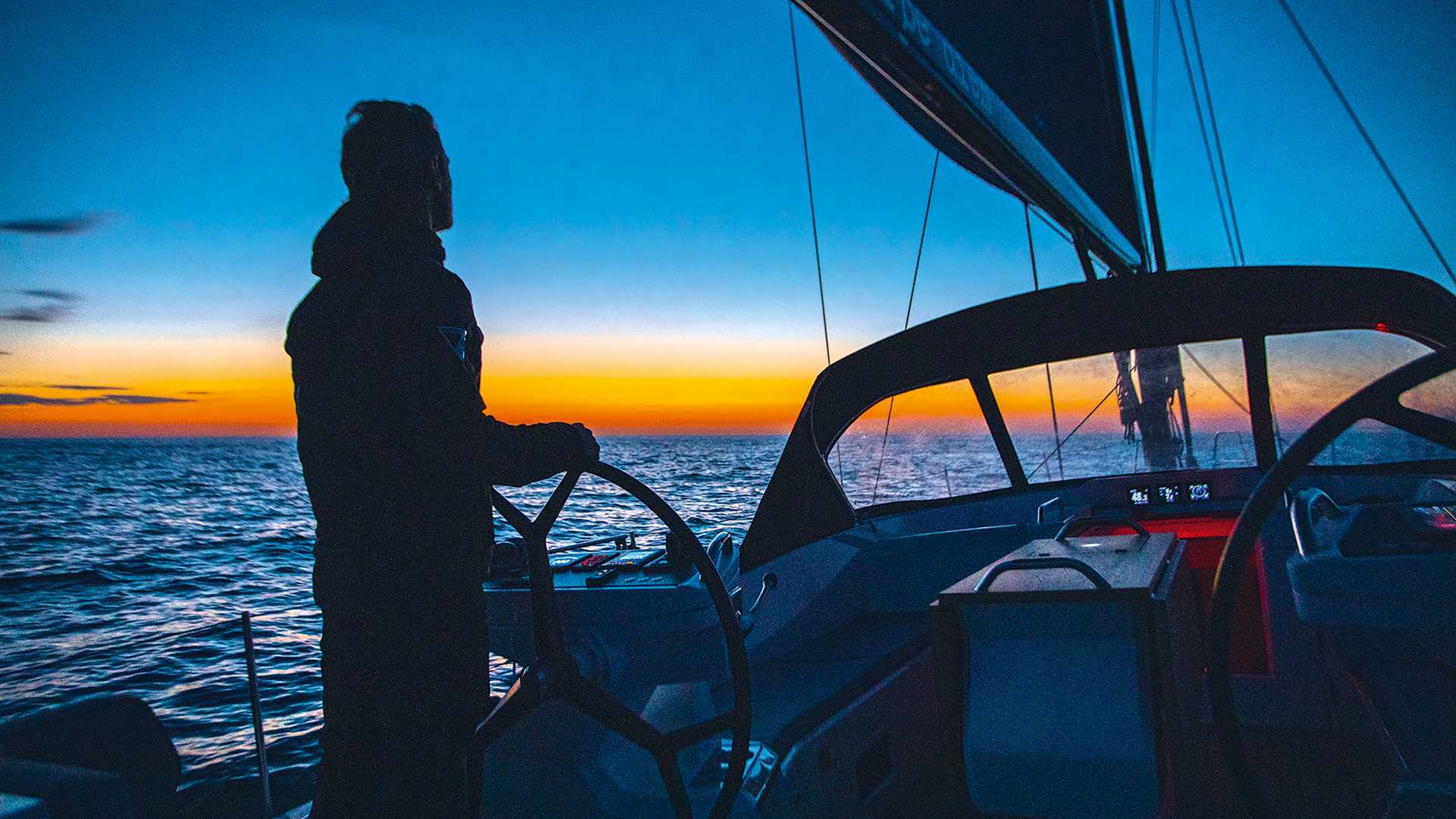 A sailor at the helm during sunset